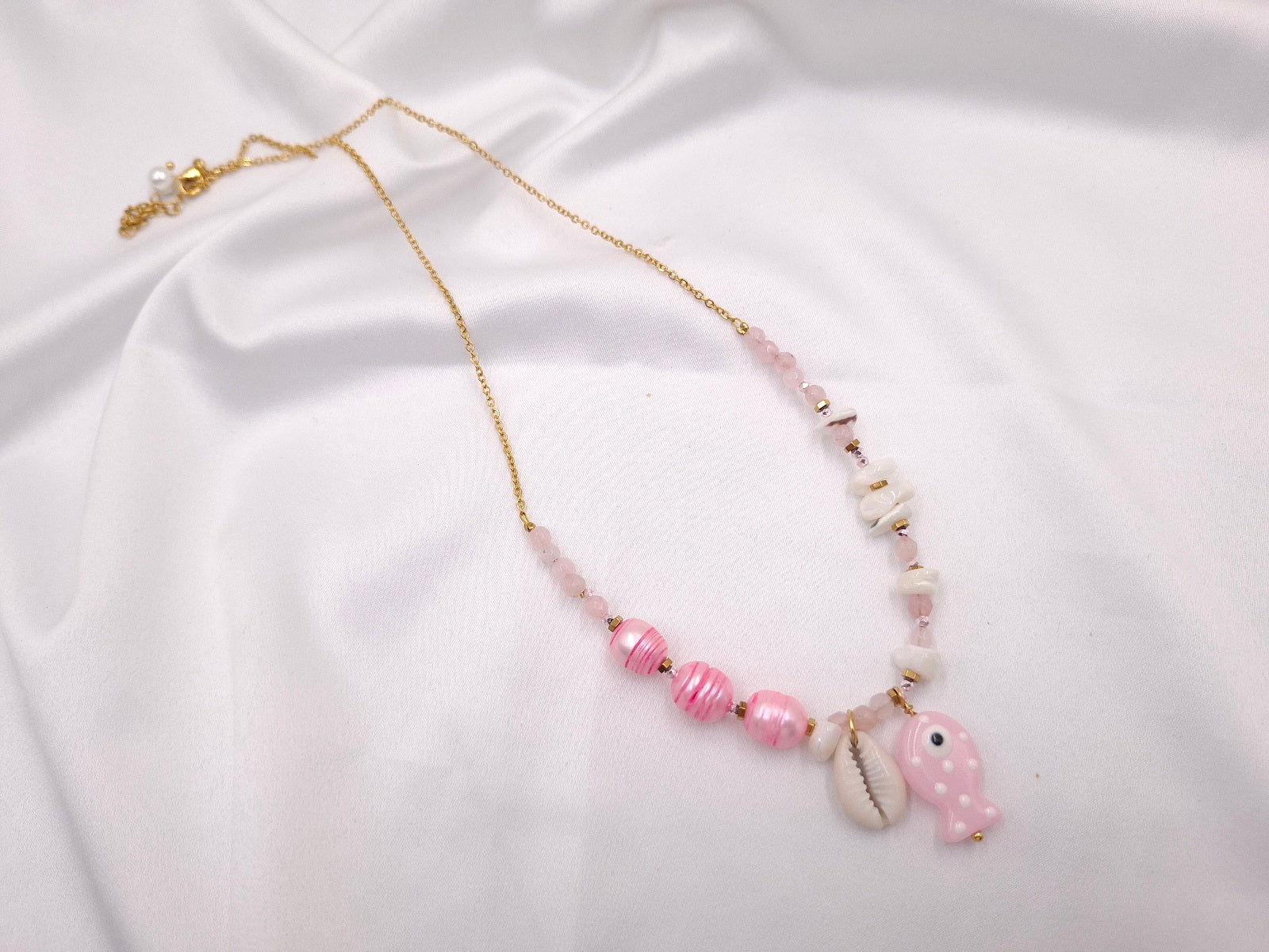 Χειροποίητο κολιέ Fish Tales Pink Shell της euhandmade με ροζ γυάλινες χάντρες, ριγέ ροζ πέρλες, γυάλινο ψαράκι, κοχύλι και χρυσαφί ατσάλινη αλυσίδα.