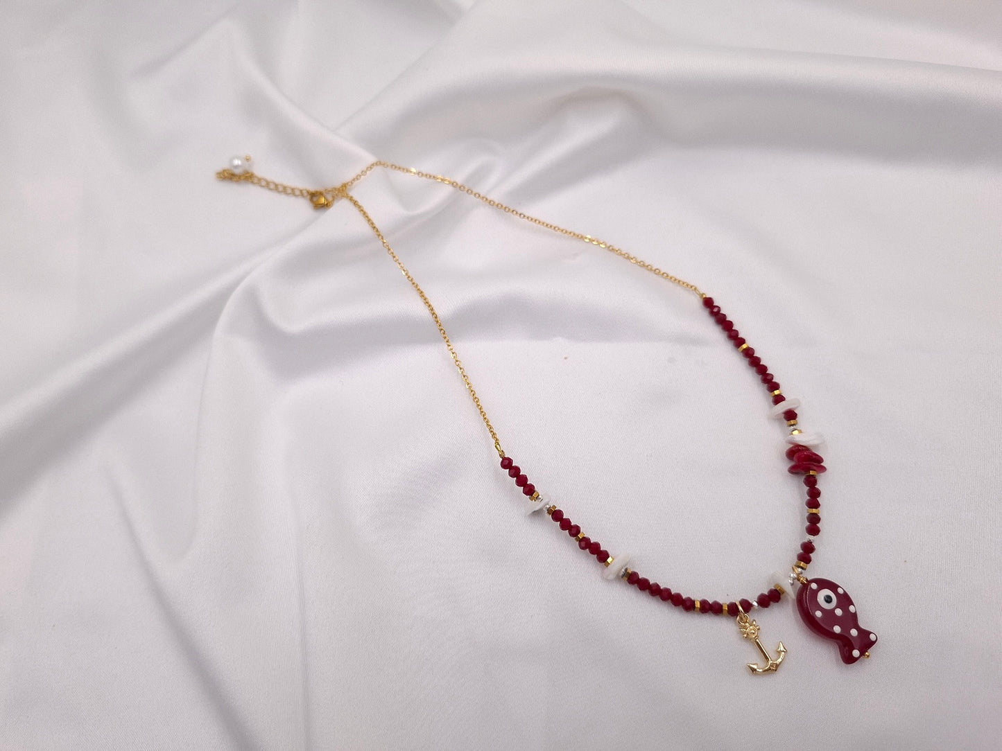 Χειροποίητο κολιέ Fish Tales Ruby Harbor της euhandmade με μπορντό κρύσταλλα, γυάλινο ψαράκι, χρυσαφί άγκυρα, λευκά κοχύλια και χρυσαφί ατσάλινη αλυσίδα.