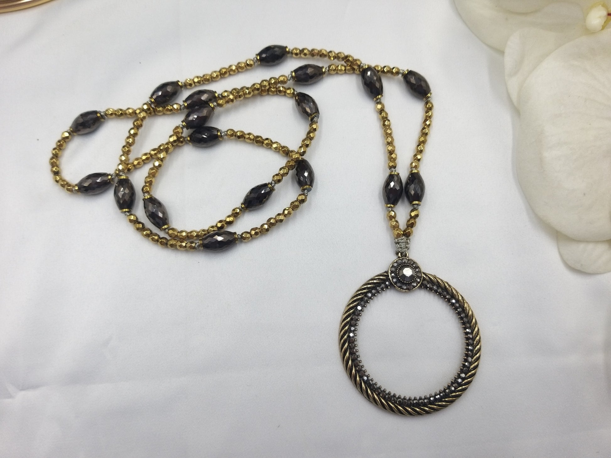 Κολιέ αιματίτη με οβάλ μεταλλικό χρυσό-μαύρο μενταγιόν πάνω σε λευκό φόντο – χειροποίητο κόσμημα euhandmade