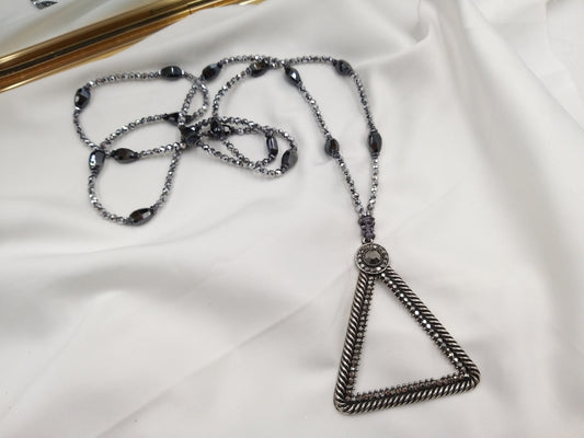 Κολιέ με αιματίτη και τριγωνικό μεταλλικό μενταγιόν πάνω σε λευκό ύφασμα – χειροποίητο κόσμημα euhandmade.