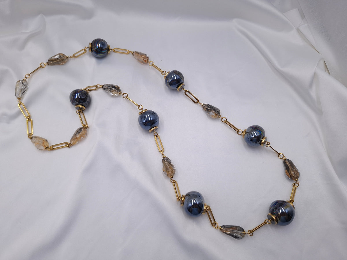 Χειροποίητο μακρύ κολιέ euhandmade με μεταλλικές μαύρες κεραμικές χάντρες 22mm με μπλε ιριδισμούς, κρύσταλλα σε σαμπανί και καπνιστές αποχρώσεις και χρυσαφί ατσάλινη αλυσίδα.