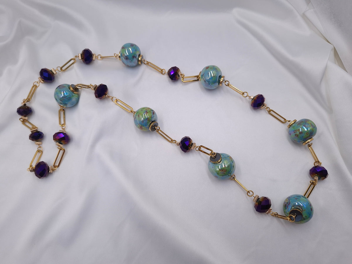 Χειροποίητο μακρύ κολιέ euhandmade με τιρκουάζ κεραμικές χάντρες 22mm, πράσινες και μωβ πινελιές, διακριτικές απαλές κίτρινες λεπτομέρειες, σκούρα μωβ ιριδίζοντα κρύσταλλα και χρυσαφί ατσάλινη αλυσίδα.
